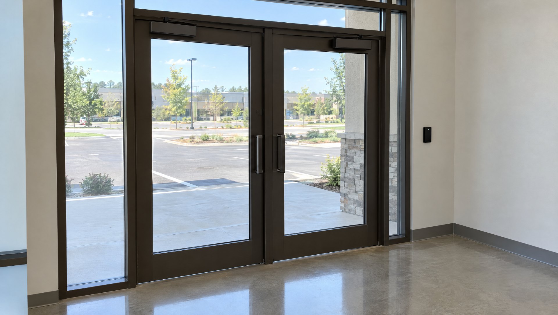 Finished dark bronze storefront entrance with a card reader on the wall and no visible wiring, the result of electrified door hardware planned before fabrication