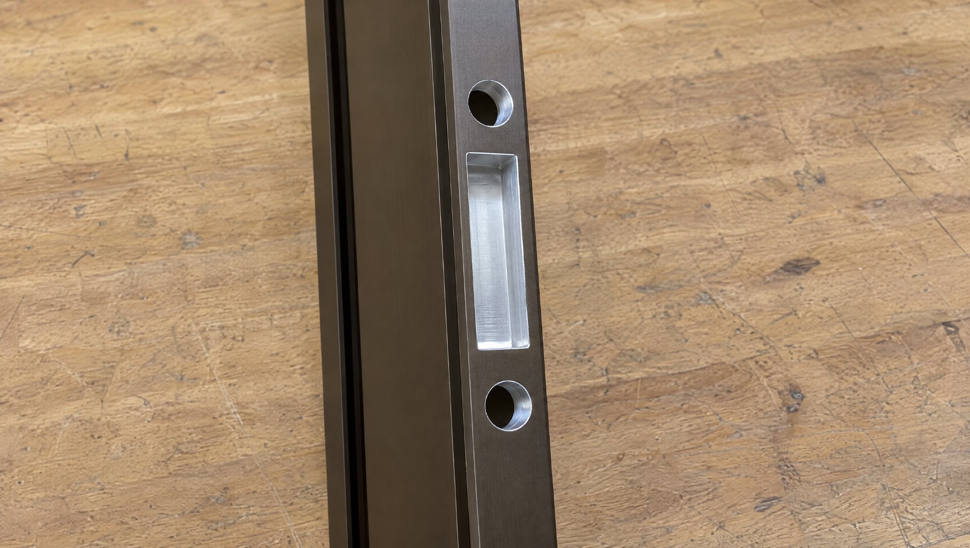 Clean rectangular mortise pocket and two pull holes machined into the lock stile of a dark bronze aluminum storefront door, hardware prep cut to the template